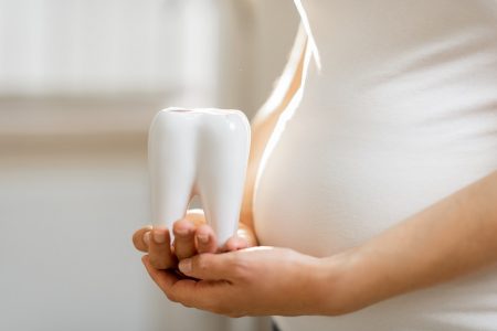 Pregnant woman holding tooth model near her belly, close-up view. Concept of a dental health during a pregnancy